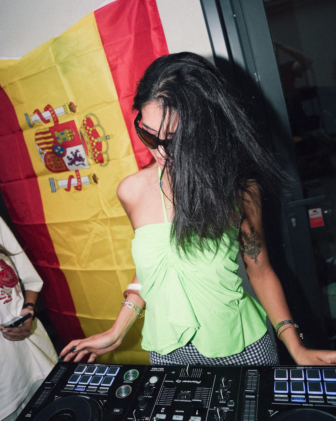 DJ in a neon green top playing in front of a Spanish flag at the Seraya AW1 party — photo by vinny.mp4, Stockholm